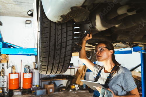 Young adult female mechanic inspecting car in auto repair shop