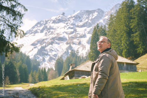 Middle age man hiking near Moleson mountain in Gruyere Switzerland with alpine chalet, forest and snowy peaks under clear sky scenic Swiss landscape