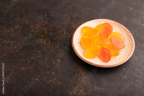 Jelly candies on ceramic plate on black concrete, side view, copy space