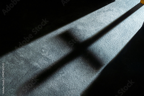 Bild auf Leinwand A dramatic shadow of a Christian cross cast onto a textured floor by a beam of l
