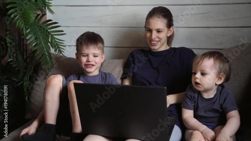 White sister and two boys watching laptop together on couch, animated faces reacting to content, little brother giggles, relaxed posture, indoor plant framing scene, gentle afternoon light, collective