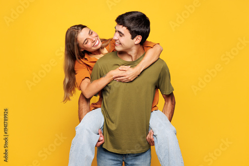 Young fun couple two friends family man woman wear shirt casual clothes together giving piggyback ride to joyful sit on back isolated on pastel plain light yellow background studio. Lifestyle concept