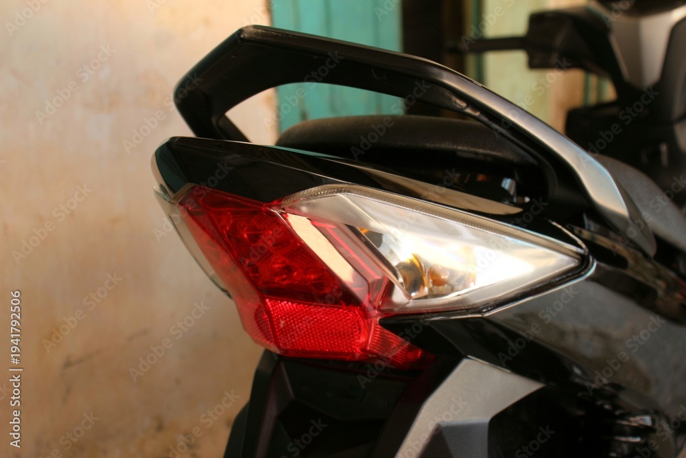 Fototapeta premium Rear close-up of a Honda motorcycle highlighting the red tail light, sleek body design, and rear handle. Captured with soft natural lighting and shallow depth of field in a garage environment