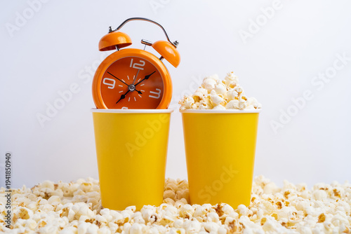 Orange alarm clock and fresh popcorn in yellow paper cups. Movie showtime concept. 