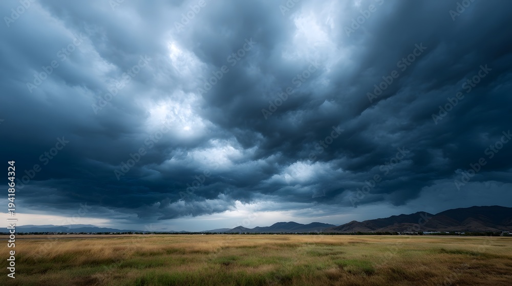 Fototapeta premium Dramatic storm clouds gather over a golden grassy plain with distant mountains