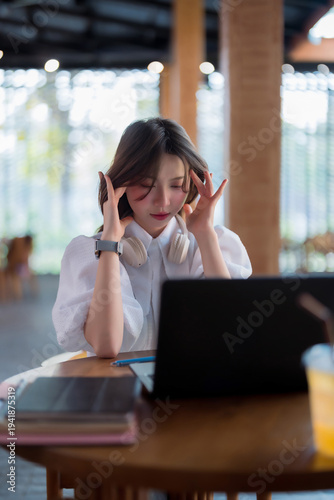 Asian young adult woman freelancer student experiencing severe work related stress headache burnout working on laptop computer in a busy cafe remote office