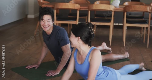 Couple practicing yoga pressing up from prone into cobra on green mats, bonding near dining table