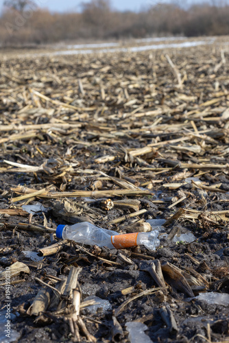 Wallpaper Mural A crushed plastic water bottle with an orange label lies in a muddy field among dry corn stalks and melting ice patches. Torontodigital.ca