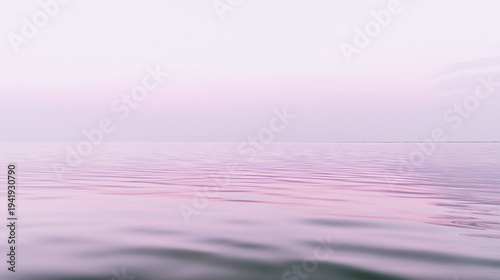 Serene landscape of calm water reflecting soft pastel colors of dawn with gentle ripples and a clear horizon line under a light pink sky