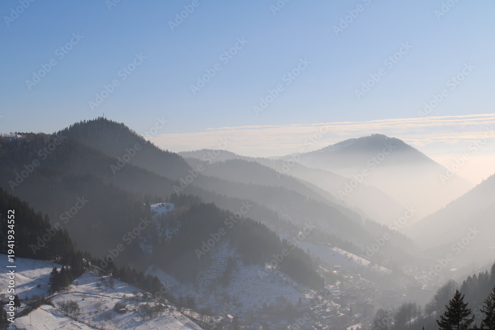 Obraz premium Panoramic view of misty mountains covered in snow during a cold winter morning
