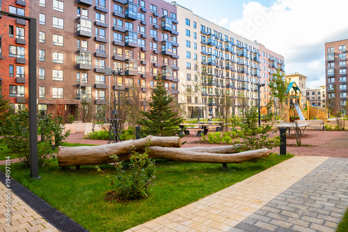Decorative landscape design with natural log in city park. Eco friendly urban furniture made of wood. Modern residential complex courtyard with green lawn and sustainable architecture.