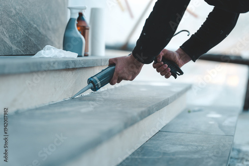 Construction worker applying sealant to outdoor stone steps with a caulking gun