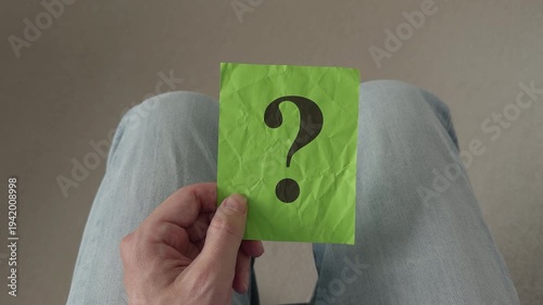 A man holding a crumpled green paper with a black question mark on it in his hand, symbolizing uncertainty and the search for answers. Close up.