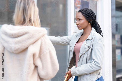 Woman talks to another person outside a store during the afternoon in an urban area
