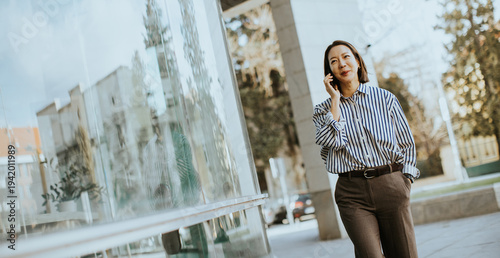 Korean woman talks on phone while walking by modern building on a sunny day