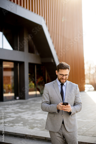 Businessman checks phone outside modern office building during daytime hours