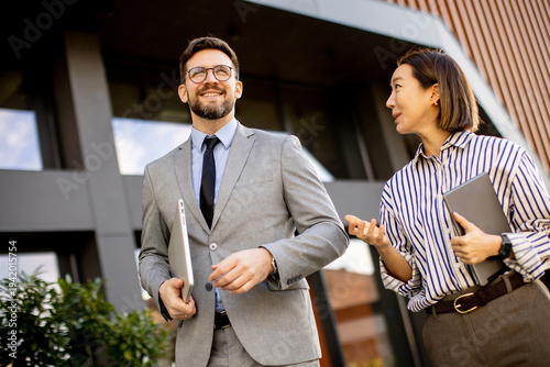 A Korean woman talks to a Caucasian man as they walk outside an office