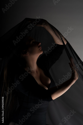 Canvas-taulu Mysterious curvy woman holding flowing black veil in dark studio, dramatic low k