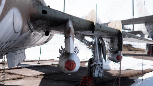 Underwing Pylons And Rocket Pods Grounded. Weathered Bomber Parked On Sunlit Tarmac With Visible Mounting Hardware, Service Cables, And Chocks Closeup Perspective Emphasizes Pylon Structure,