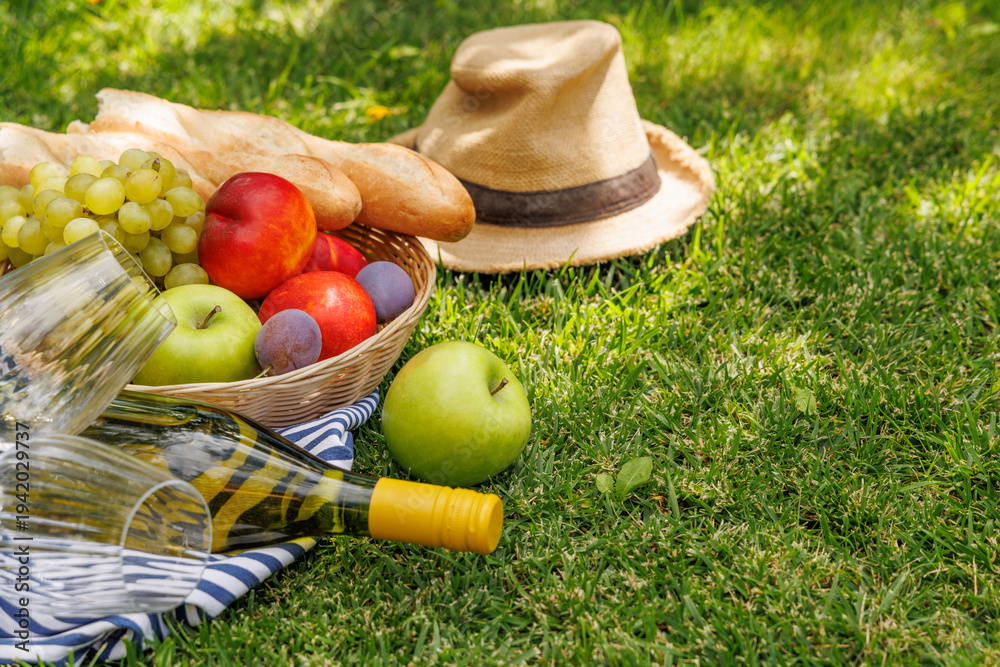 Fototapeta premium Picnic with wine, fruits, and baguette on a green meadow
