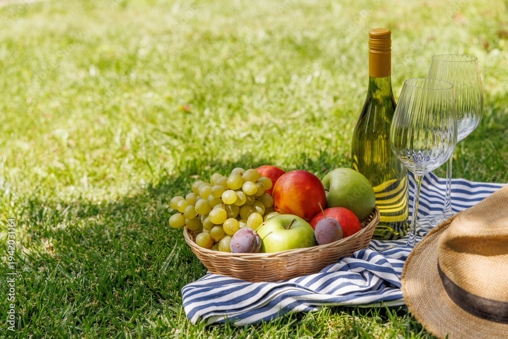 Fototapeta premium Picnic with wine, fruits, and baguette on a green meadow