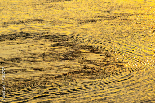 Foto Pattern formd by swirling waters of the sea with the reflection of the sun at su