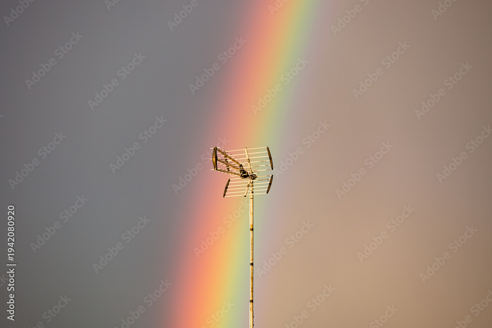 Obraz premium Vibrant Vertical Rainbow Over European Rooftops with Antenna at Golden Hour