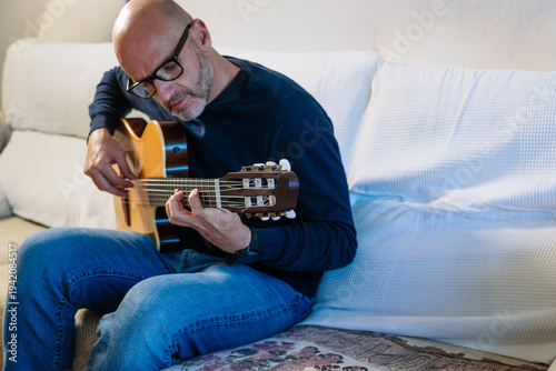 Mid adult man enjoying playing acoustic guitar at home