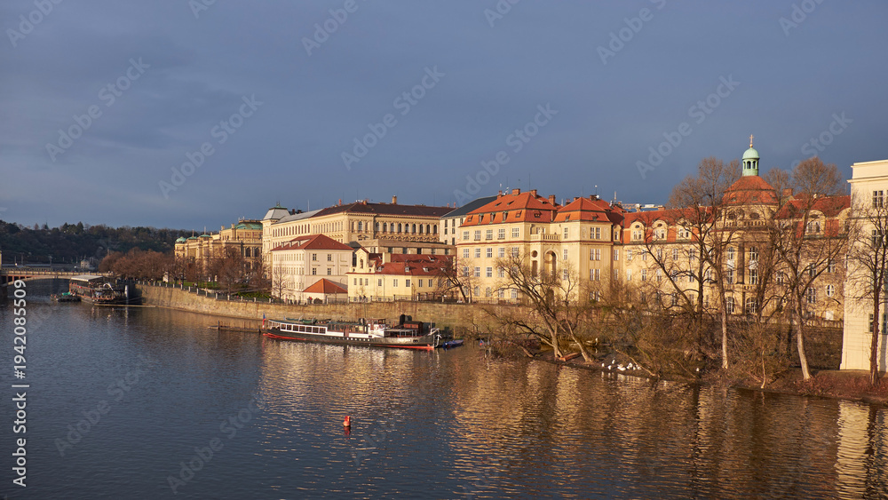 Obraz premium Vltava River with Mala Strana riverside and historic red-roofed buildings at dusk