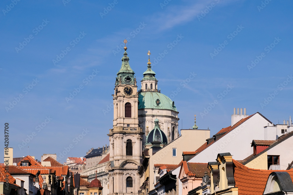 Obraz premium St Nicholas Church Prague with copper dome rising above red rooftops and blue sky