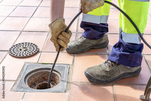 Sewer worker unclogging blocked yard drain with hydro jetting hose.