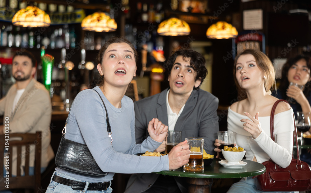 Obraz premium Group of young sports fans upset and worrying during game match on TV in big beer pub