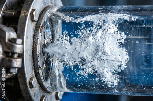 Extreme close-up of violent water cavitation bubbles inside a heavy industrial transparent glass pipe