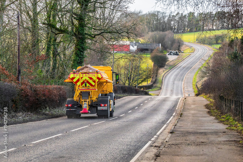 Quadro su tela Gritting truck spreading salt on winding rural countryside road in winter