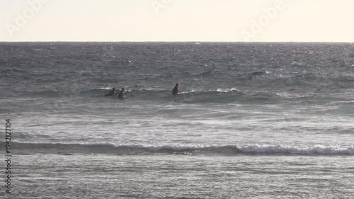 surfers waiting in the ocean, sitting on their boards and watching the horizon as gentle waves roll in under soft coastal light during a calm moment before the next set forms