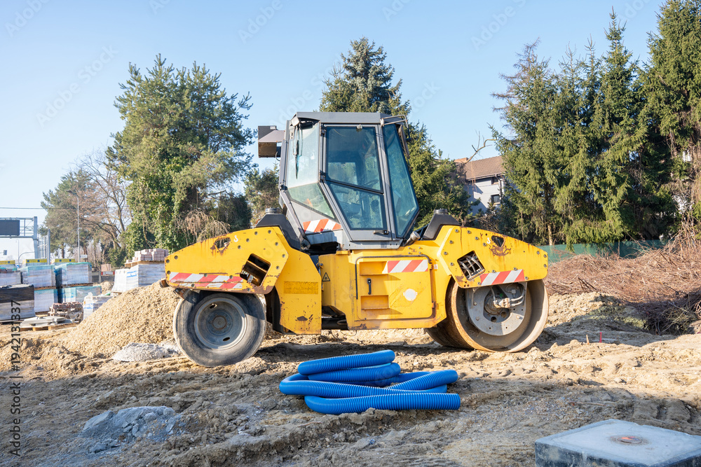 Obraz premium A yellow road roller at a construction site next to a blue corrugated pipe