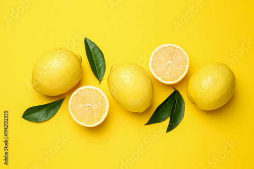 Ripe lemons and leaves on yellow background, flat lay