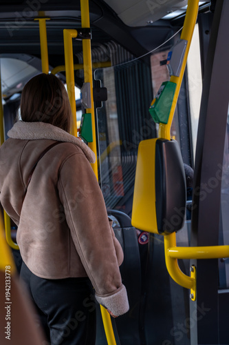 фотографія Young woman passenger traveling by modern city bus during winter, standing in the aisle
