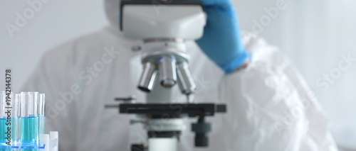 Fotografi A medical virologist in protective gear and blue gloves examines viral samples u