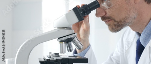 Εκτύπωση καμβά Adult male scientific researcher analyzing sample through microscope, wearing protective gear in high tech laboratory environment