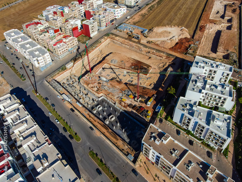 Aerial drone view of a large residential real estate development and construction site with cranes, foundations, and heavy machinery in Agadir, Morocco.