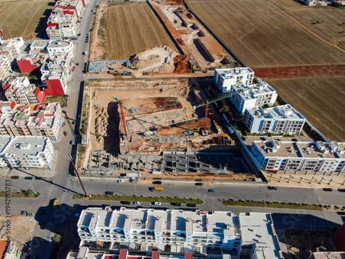 Aerial drone view of a large residential real estate development and construction site with cranes, foundations, and heavy machinery in Agadir, Morocco.