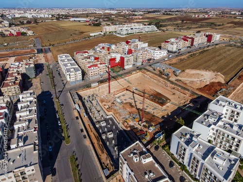 Aerial drone view of a large residential real estate development and construction site with cranes, foundations, and heavy machinery in Agadir, Morocco.