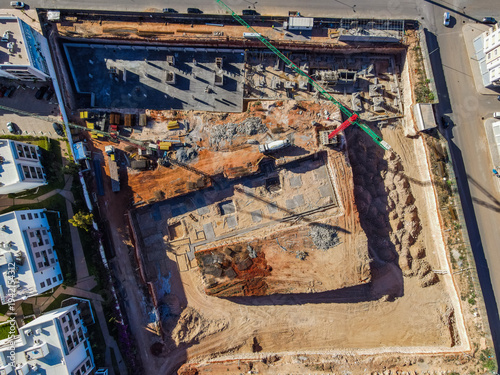 Aerial drone view of a large residential real estate development and construction site with cranes, foundations, and heavy machinery in Agadir, Morocco.