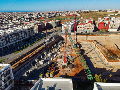 Aerial drone view of a large residential real estate development and construction site with cranes, foundations, and heavy machinery in Agadir, Morocco.