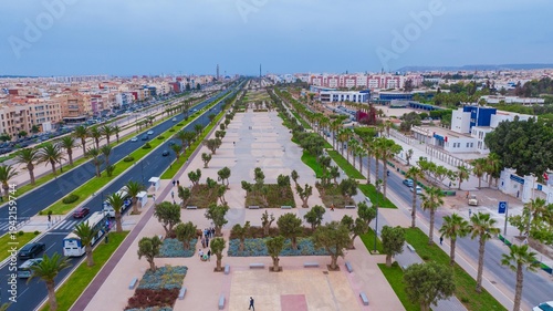 Aerial drone view of a newly renovated modern avenue featuring green public parks, sports courts, palm trees, and urban infrastructure in Agadir, Morocco.