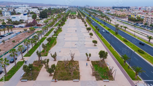 Aerial drone view of a newly renovated modern avenue featuring green public parks, sports courts, palm trees, and urban infrastructure in Agadir, Morocco.