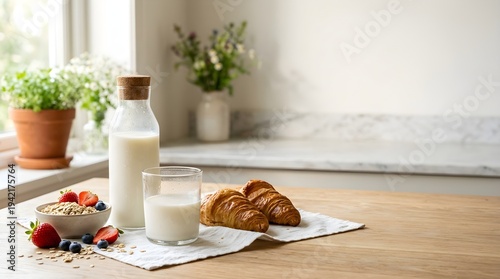 Morning breakfast milk. Glass bottle and cup of fresh milk with croissants, oatmeal, and berries on a wooden table in a kitchen setting for nutrition and morning meal concepts.