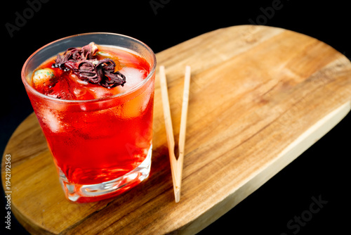 Fotografie Refreshing Red Hibiscus Mocktail with Ice Cubes and Dried Flower Garnish on Wood