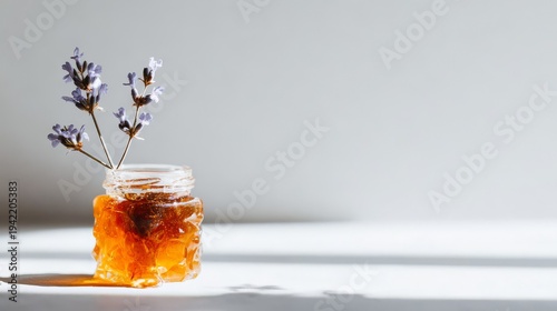 Jar of viscous amber honey with delicate flowering stem